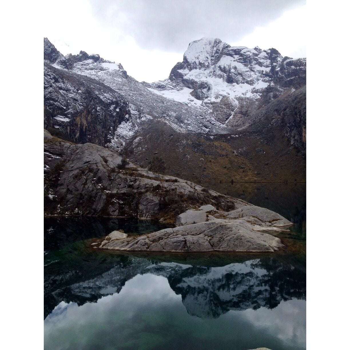 A mountain lake with snow-capped peaks and rocky terrain.