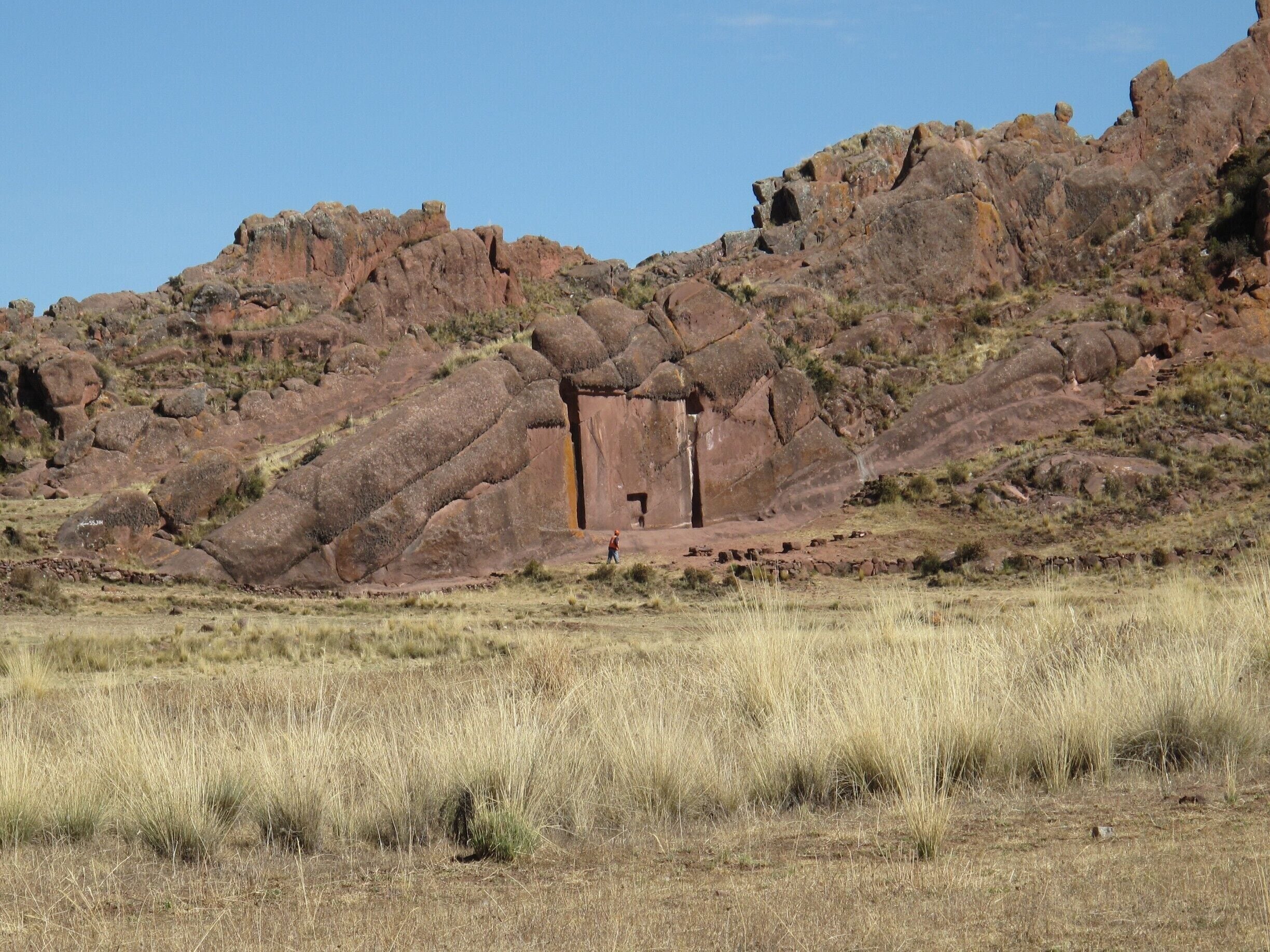 A large rock formation with a cave entrance, surrounded by dry grassland and sparse vegetation.