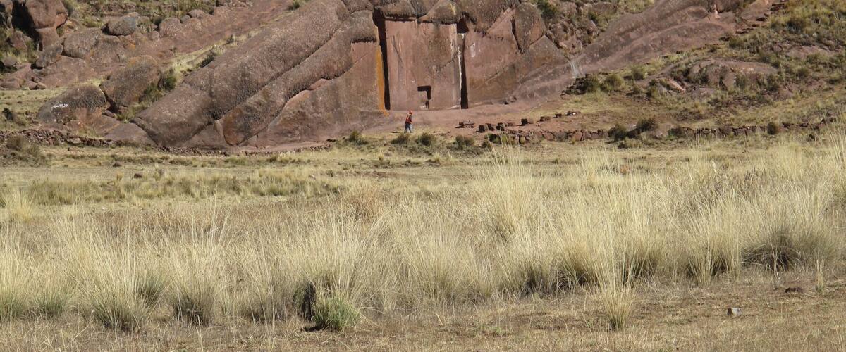 A large rock formation with a cave entrance, surrounded by dry grassland and sparse vegetation.