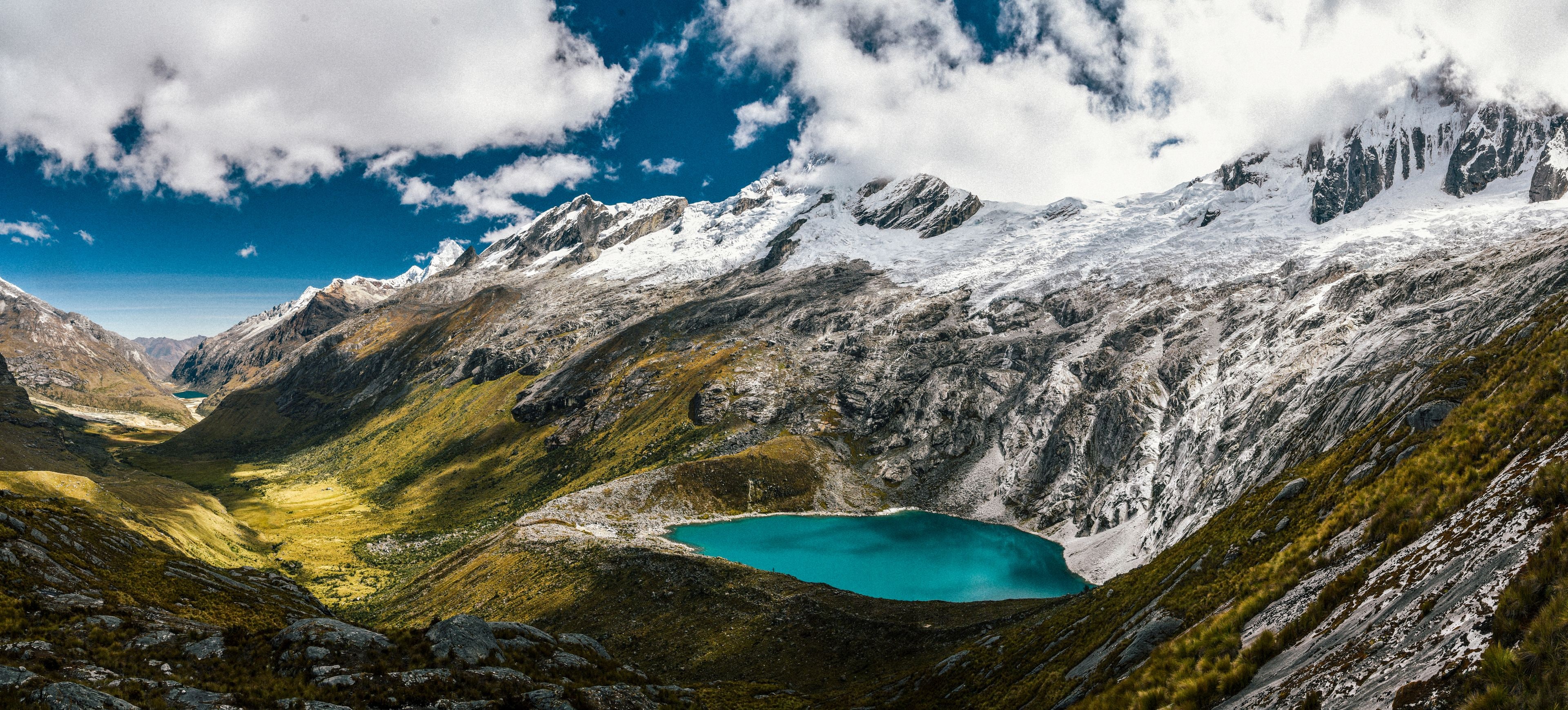 Een bergachtig landschap met een turquoise meer gelegen in een vallei, omringd door besneeuwde toppen en rotsachtig terrein.