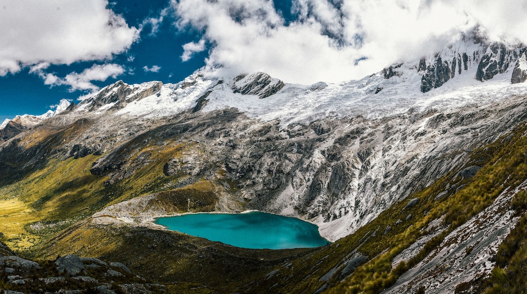 Een bergachtig landschap met een turquoise meer gelegen in een vallei, omringd door besneeuwde toppen en rotsachtig terrein.
