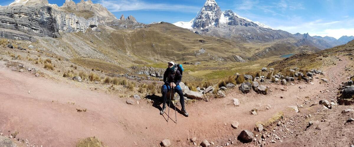 A hiker on a rocky trail with a mountain range in the background.