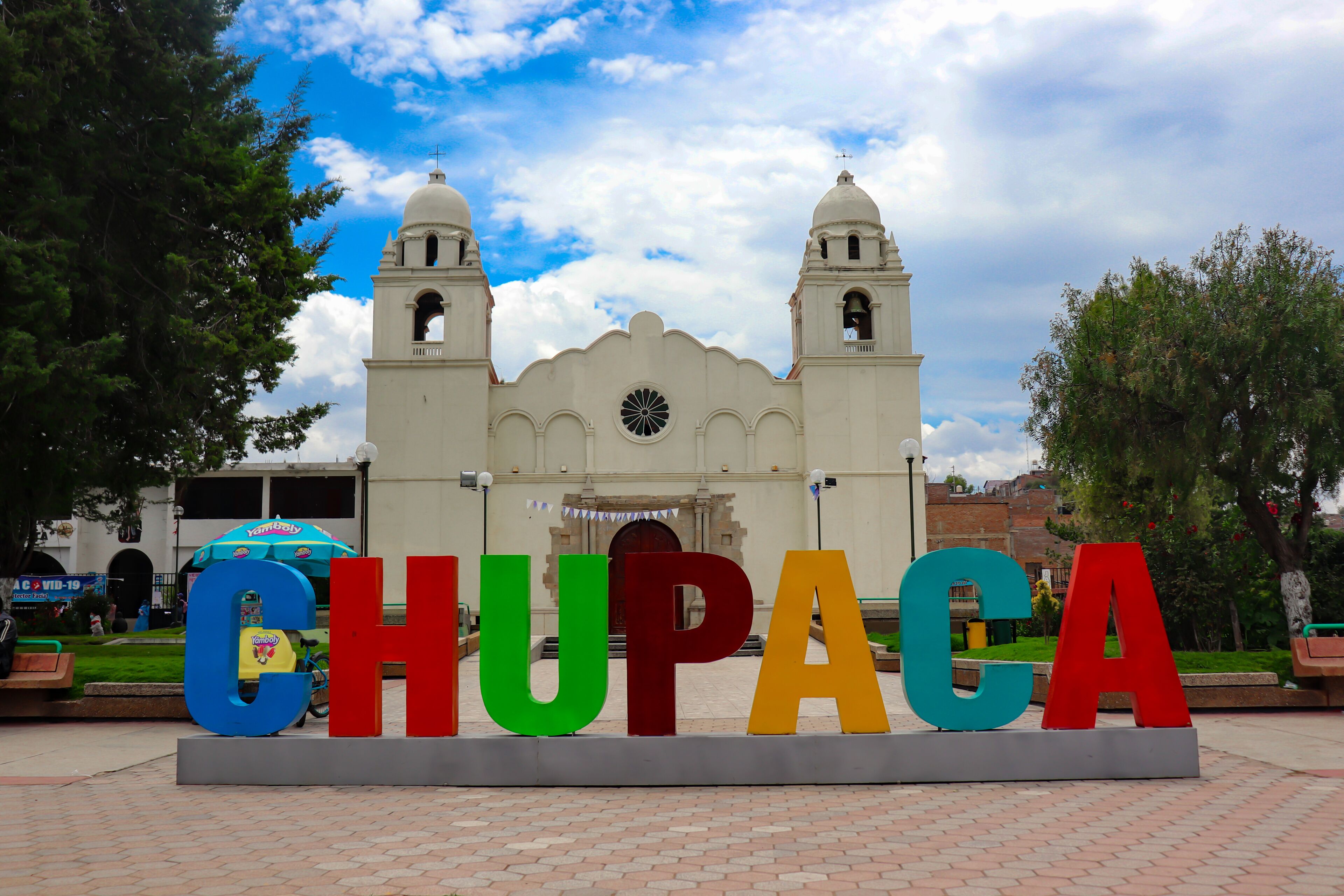 A large sign spelling "CHUPACA" in colorful letters, with a historic church in the background.