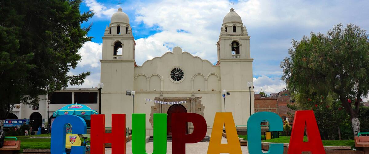 A large sign spelling "CHUPACA" in colorful letters, with a historic church in the background.