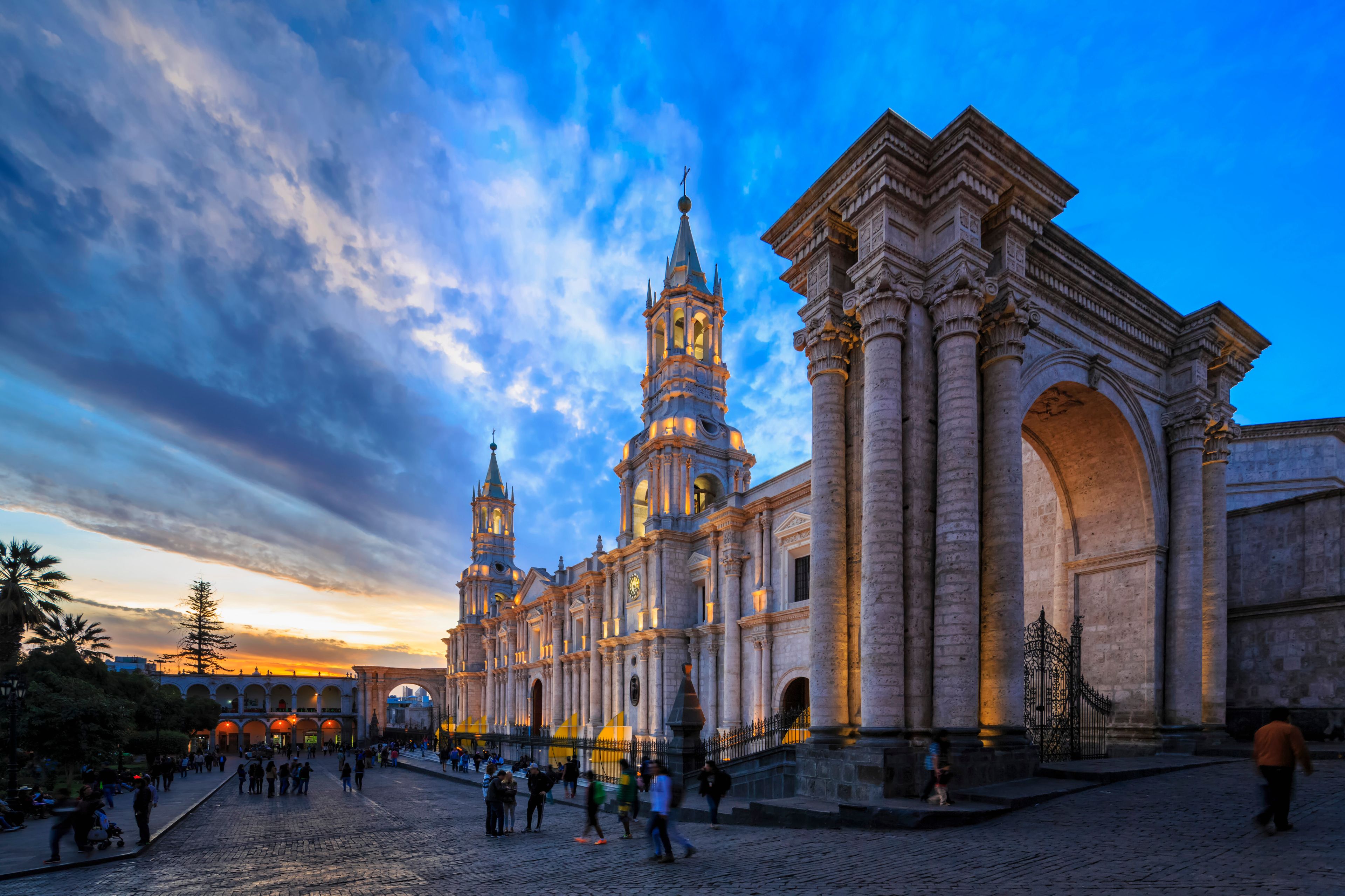 Una catedral histórica con dos torres gemelas y un gran arco, rodeada por una plaza empedrada con gente.