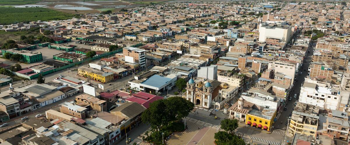 An aerial view of a densely populated city with a mix of modern and traditional architecture, a prominent church, and a large open area in the center.