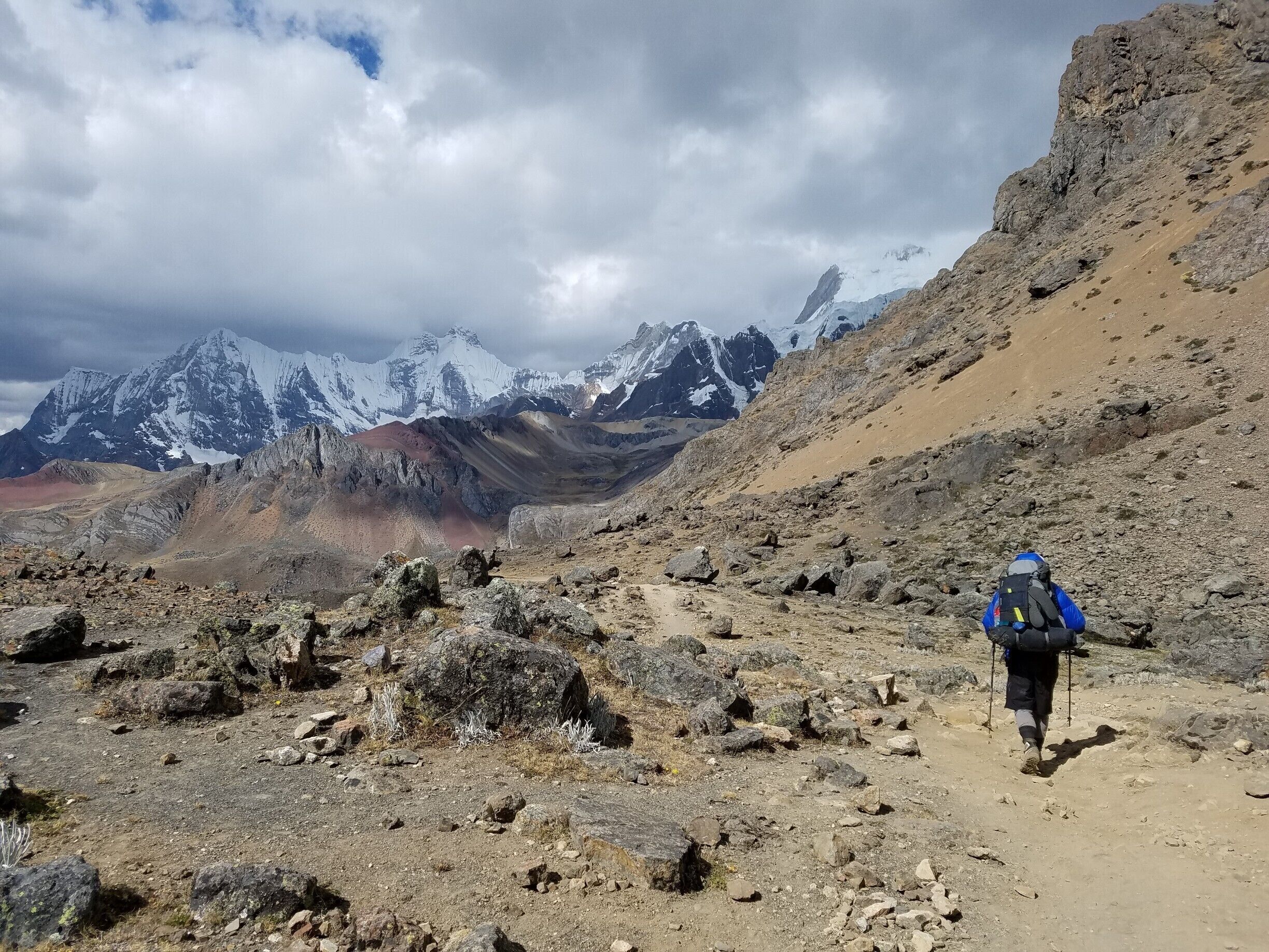 A rocky mountain trail with a hiker carrying a backpack.