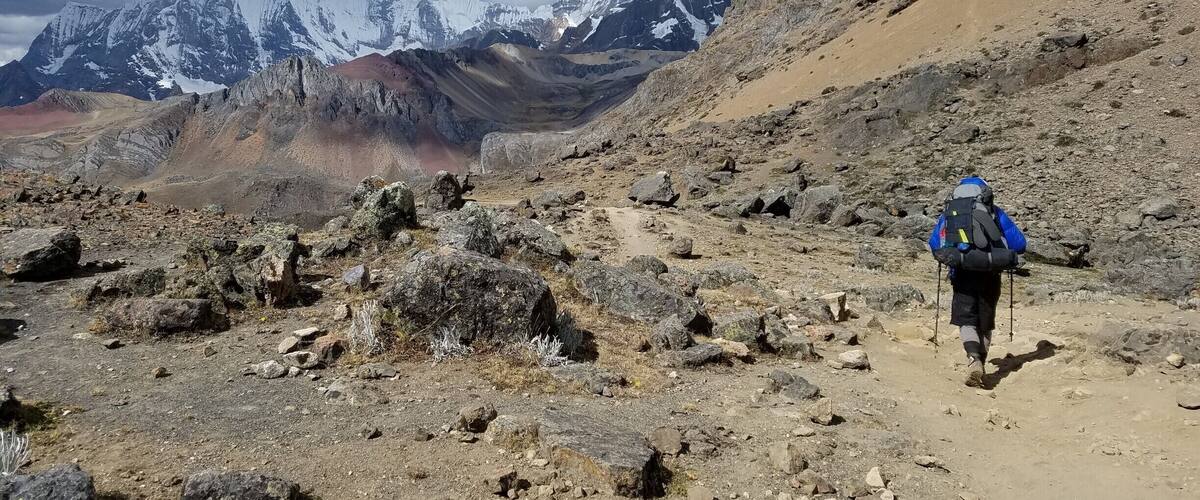 A rocky mountain trail with a hiker carrying a backpack.