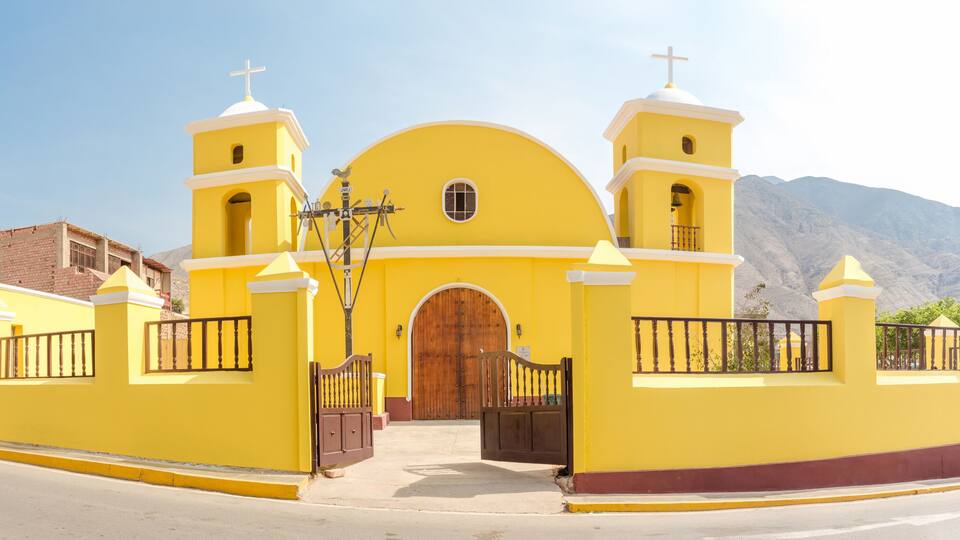 A yellow church with two towers and a large wooden door.