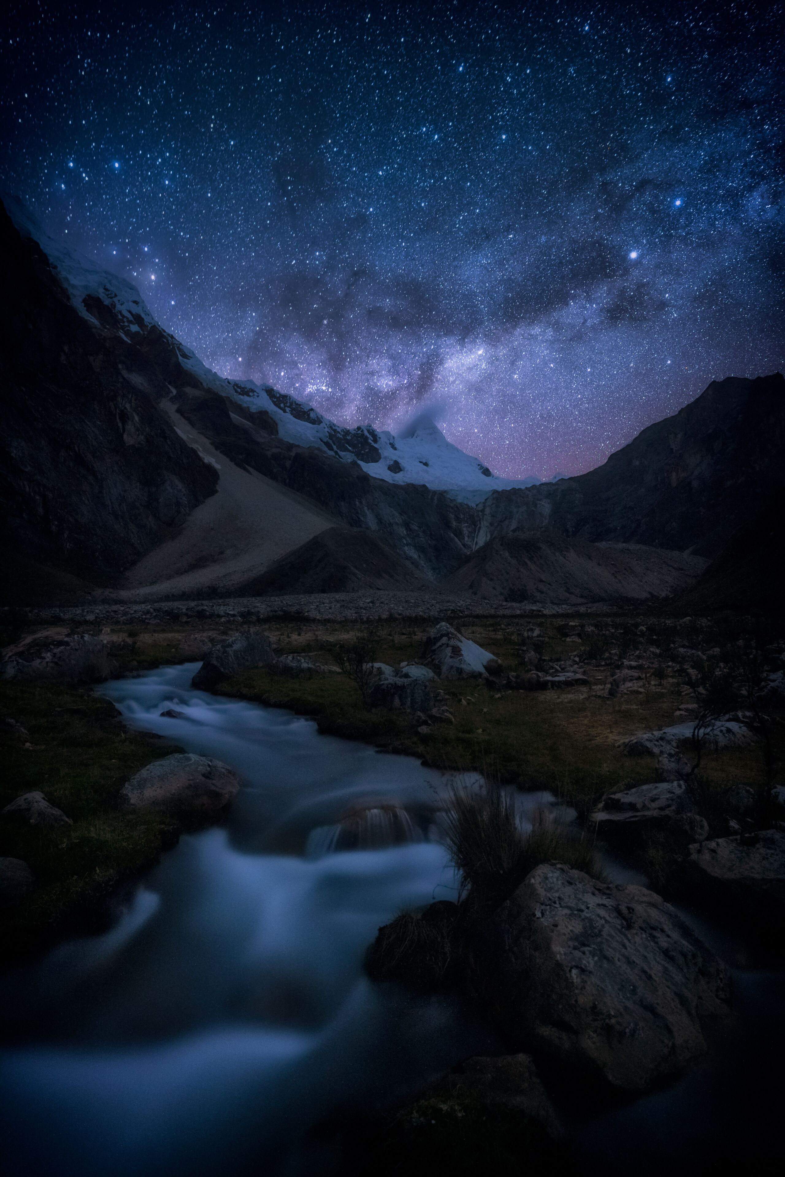 A starry night sky over a mountainous landscape with a flowing river.