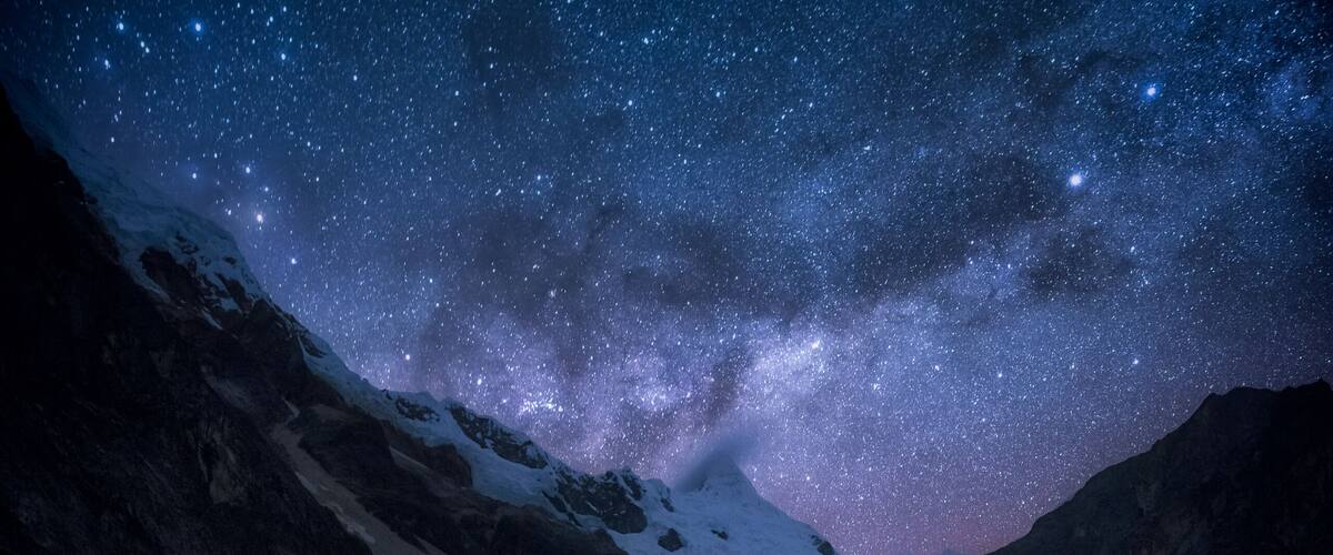 A starry night sky over a mountainous landscape with a flowing river.