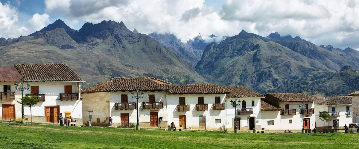 A village with white buildings and red-tiled roofs, surrounded by mountains.