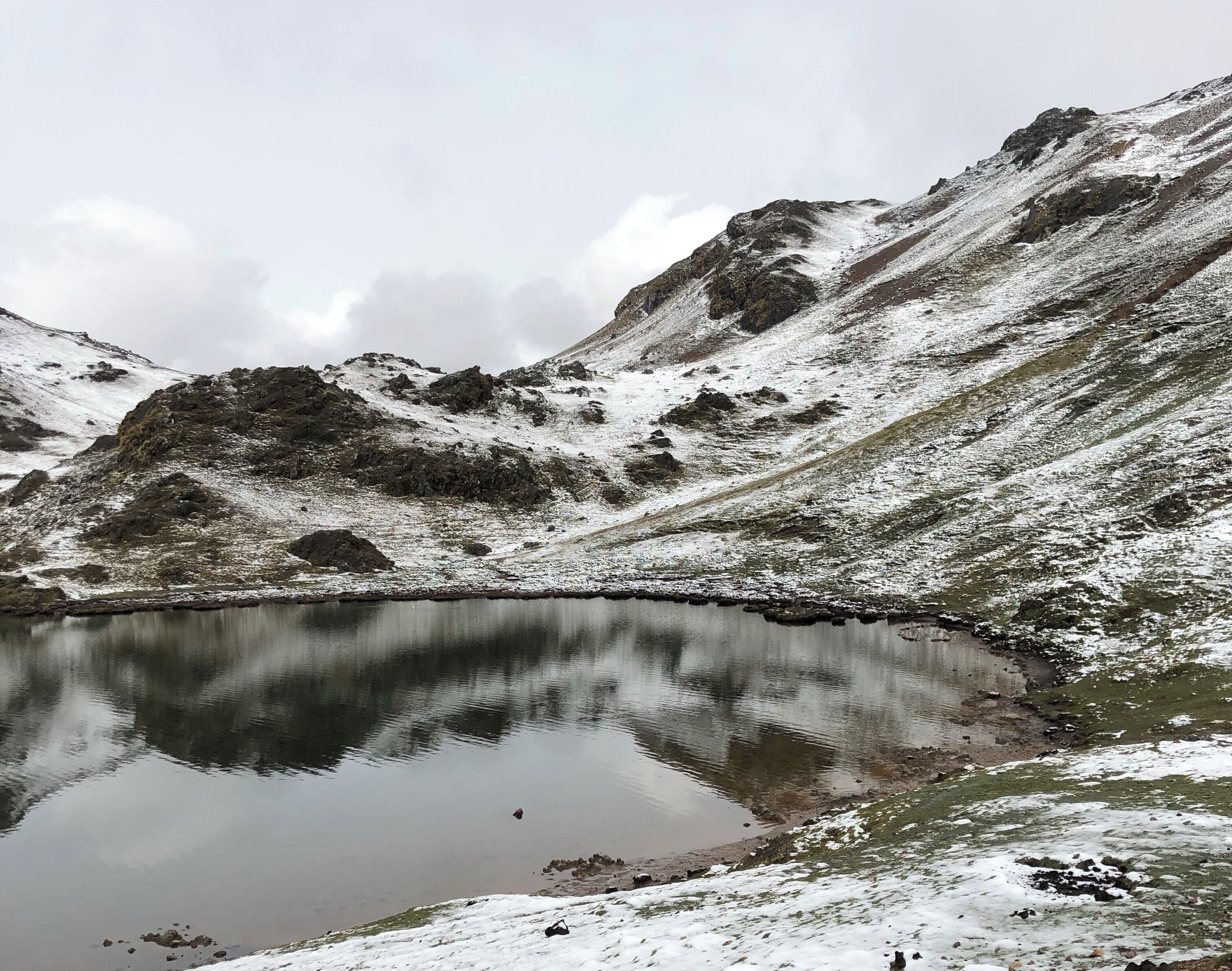A snow-covered mountain with a lake reflecting the rocky terrain.