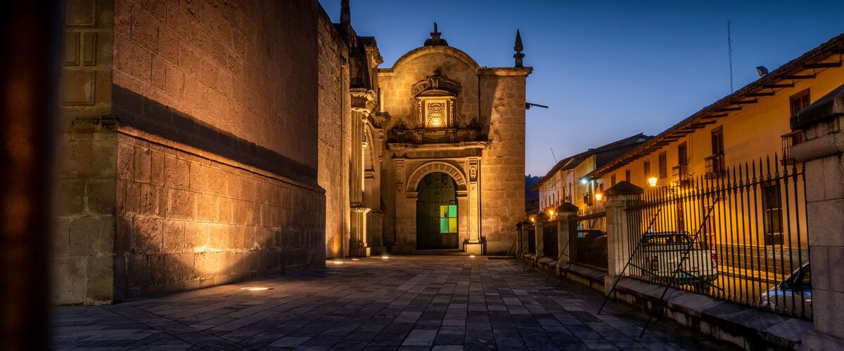 A historic building with a large arched entrance and a bell tower at dusk.