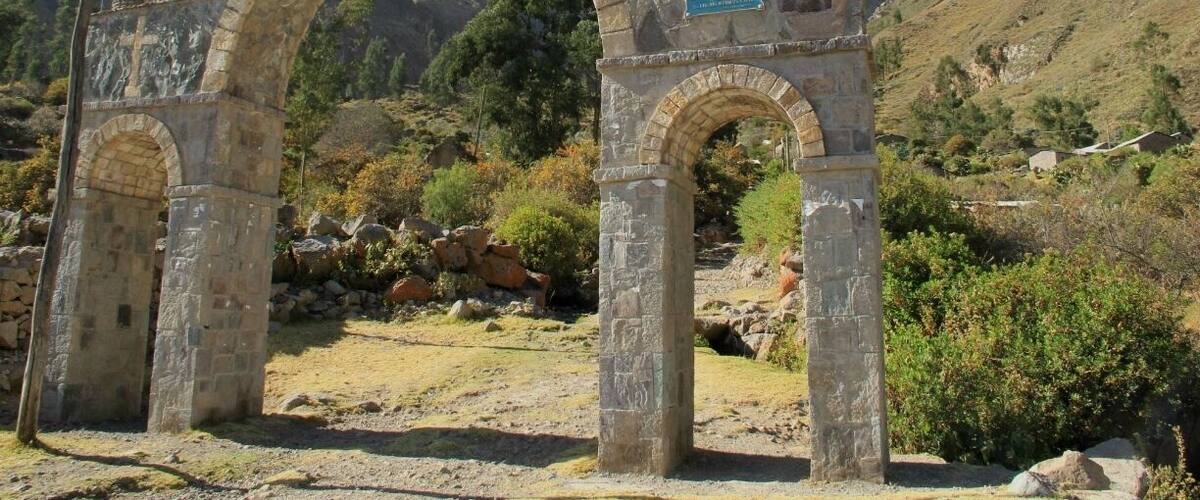 An ancient stone archway with inscriptions, set against a mountainous backdrop.