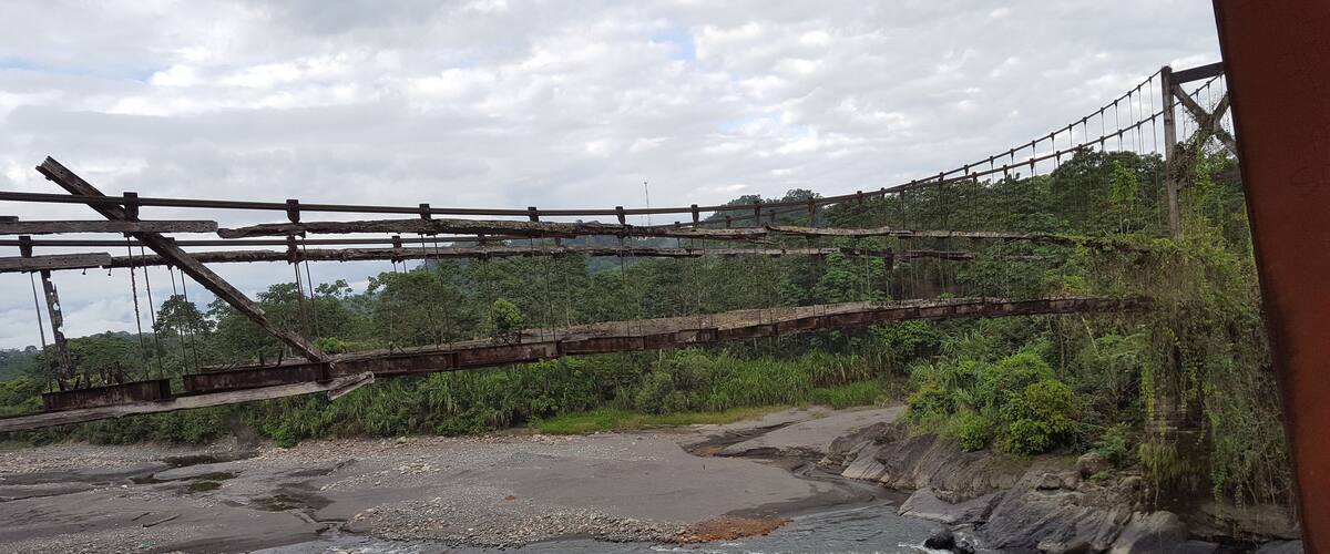 A suspension bridge over a river with rocky banks and dense greenery.