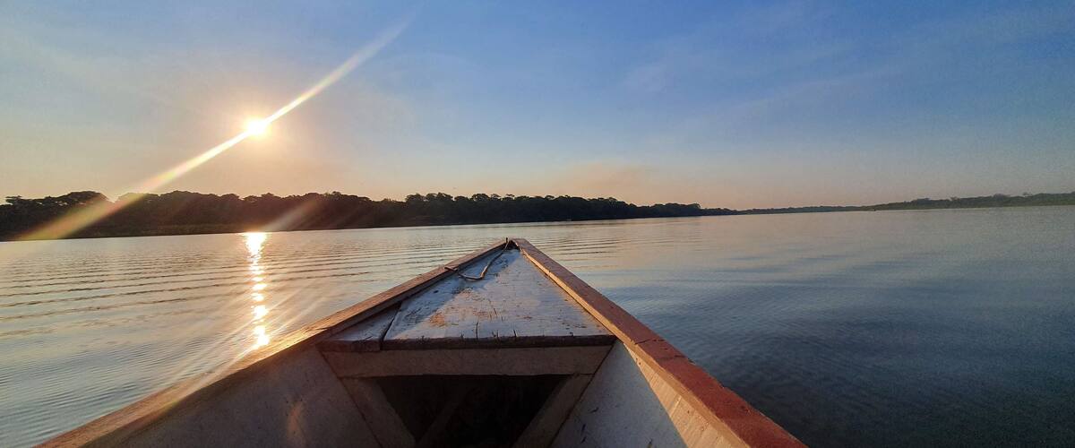 A boat on calm water with the sun low on the horizon, reflecting on the surface.