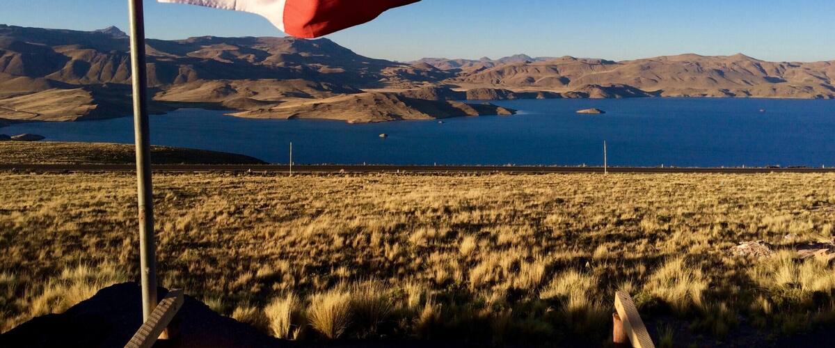 A flag on a pole with a mountainous landscape and a body of water in the background.