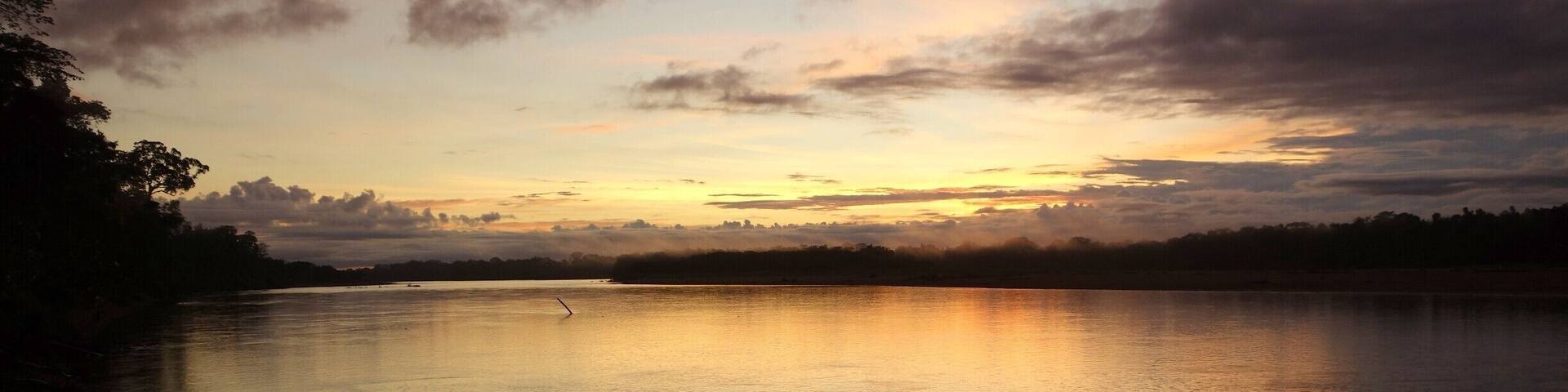 A calm lake at sunset with boats docked on the shore.