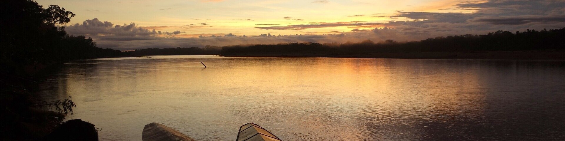 A calm lake at sunset with boats docked on the shore.