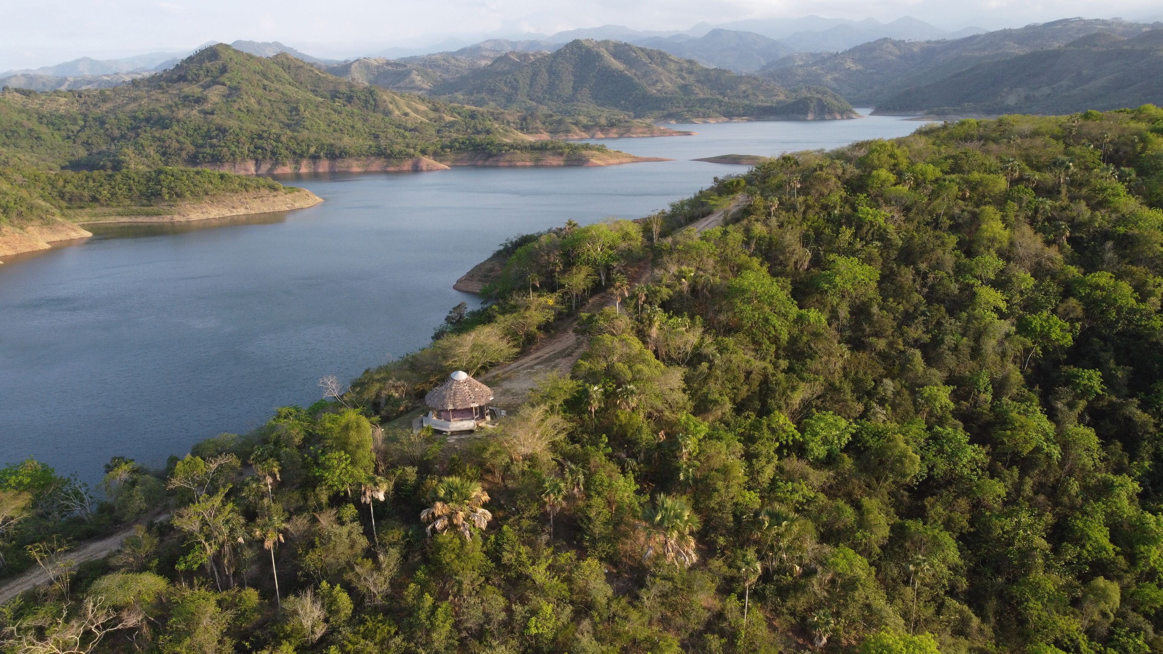 A river winding through a mountainous landscape with dense greenery and a small hut by the water's edge.