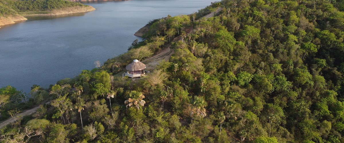 A river winding through a mountainous landscape with dense greenery and a small hut by the water's edge.