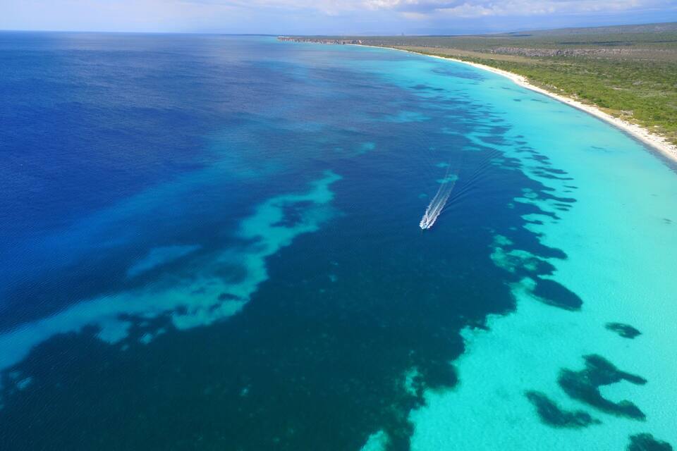 A coastal landscape with a clear blue sea, a sandy beach, and a ship in the water.