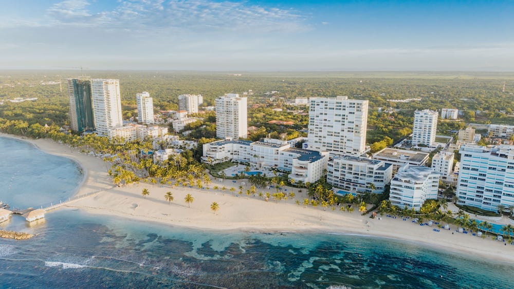 Aerial view of the coastal resort area of Juan Dolio, featuring high-rise buildings, sandy beaches, palm trees, and turquoise waters in Juan Dolio, San Pedro de Macoris, Dominican Republic.