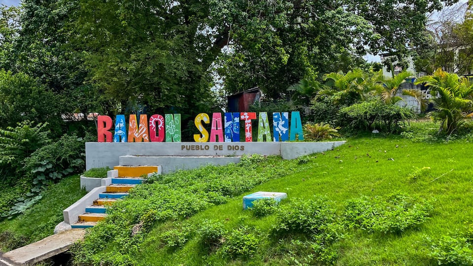 A colorful sign with the text 'RIO SANTA' and 'PUEBLO DE DÍAS' in a lush green setting.