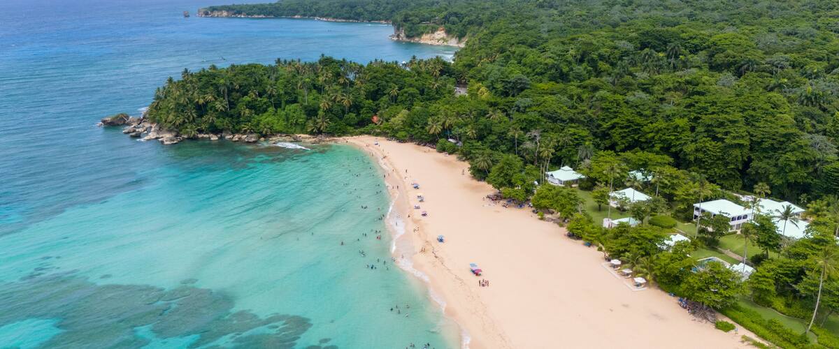 A tropical beach with clear turquoise waters, a sandy shore, and lush green hills in the background.