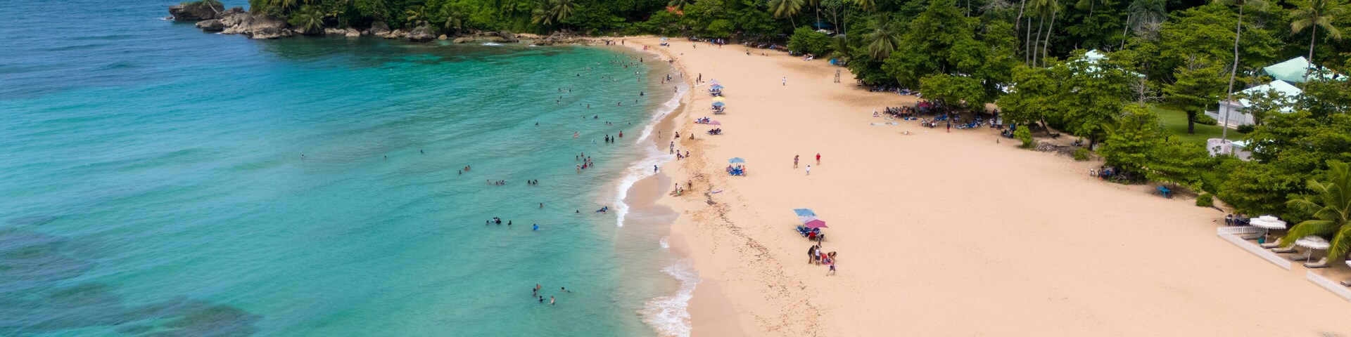 Uma praia tropical com águas turquesa cristalinas, uma faixa de areia e vegetação verde exuberante no morro.