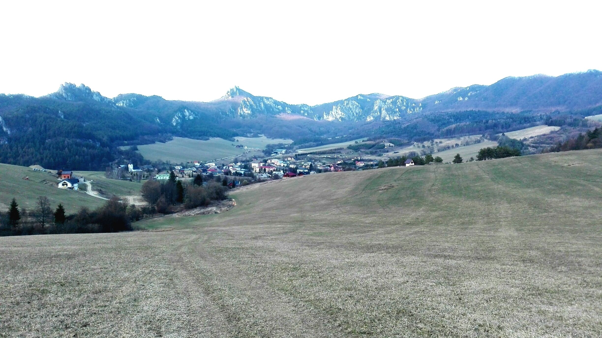 A rural landscape with a small village nestled in a valley, surrounded by mountains.