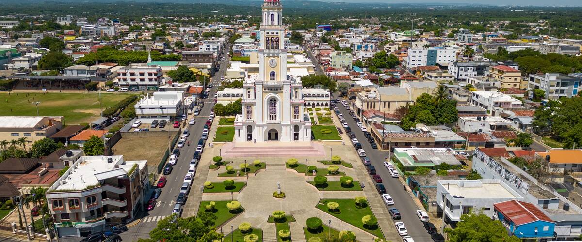 An aerial view of a city with a prominent church featuring a red dome, surrounded by a mix of residential and commercial buildings, and a green park in the center.