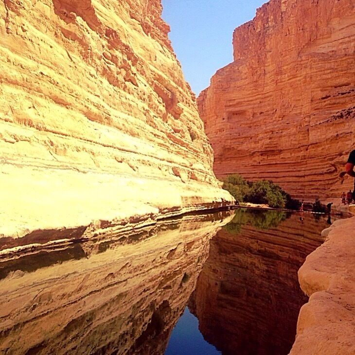 A canyon with layered rock formations and a calm river reflecting the cliffs.