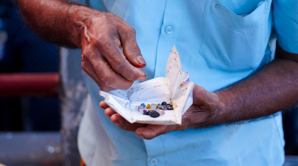 An individual at the Nivithigala gem market in Sri Lanka presents a collection of rough gemstones wrapped in paper for evaluation. He is negotiating with another person to secure a better price.