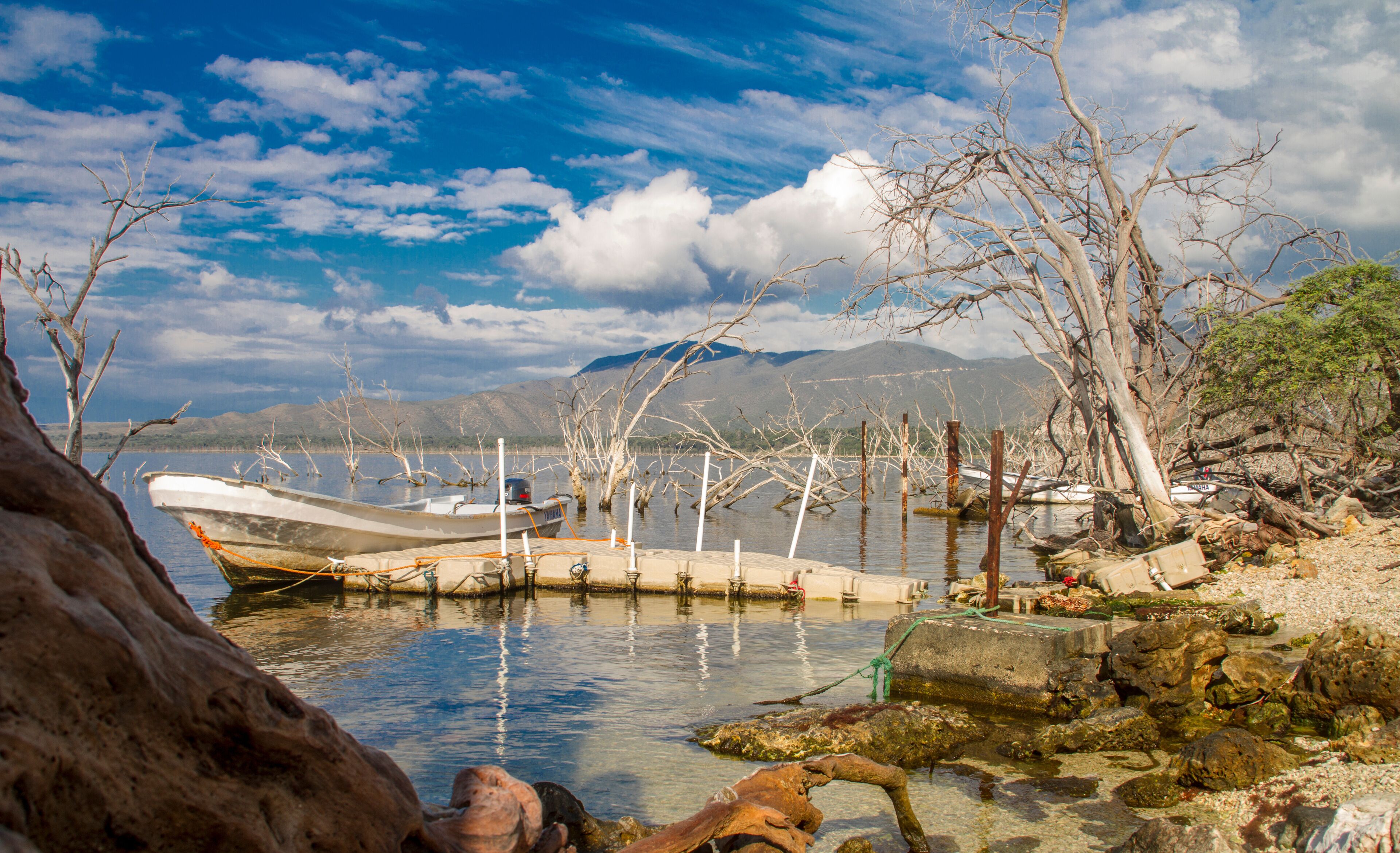 A lake with boats, rocky shore, and mountains in the background.