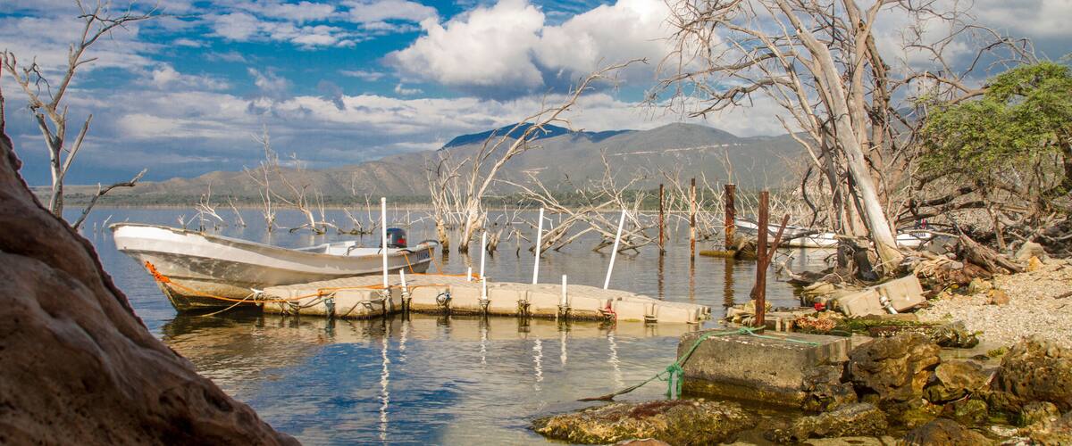 A lake with boats, rocky shore, and mountains in the background.