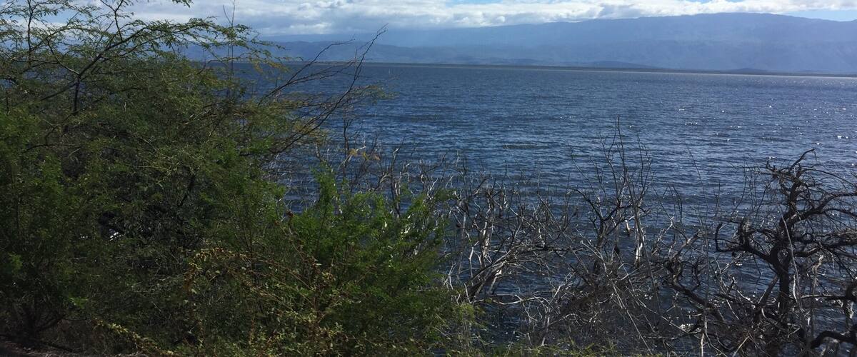 A clear blue sky, calm sea, and distant mountains.