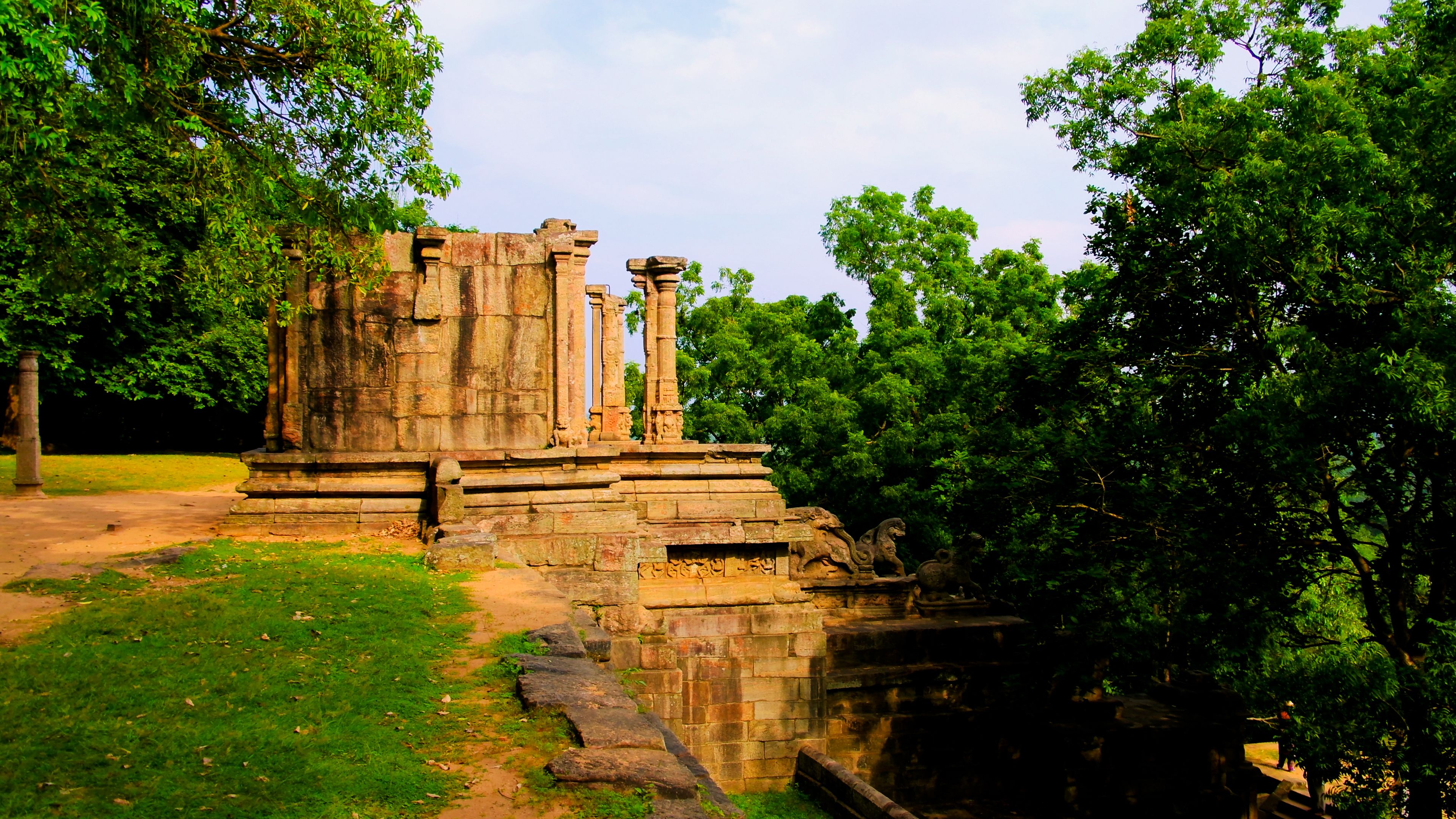 Ancient stone ruins with columns and a water feature, surrounded by lush greenery.