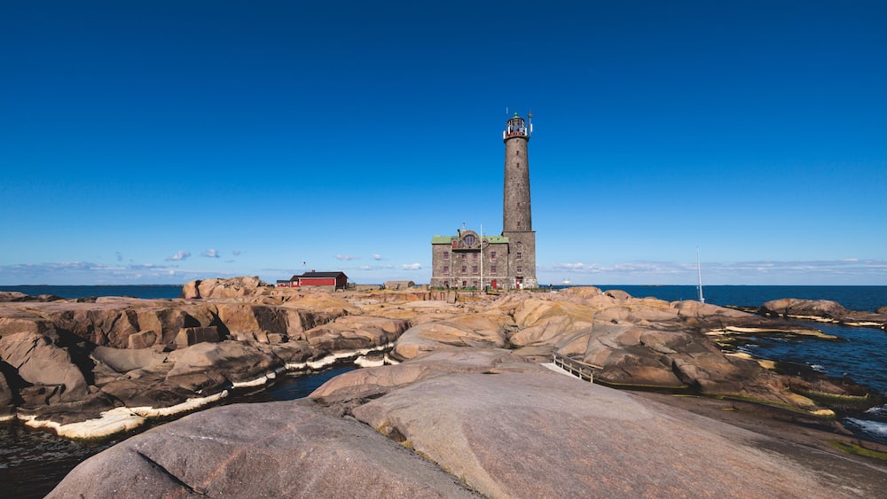 Ein Leuchtturm auf felsigem Gelände vor blauem Himmel.