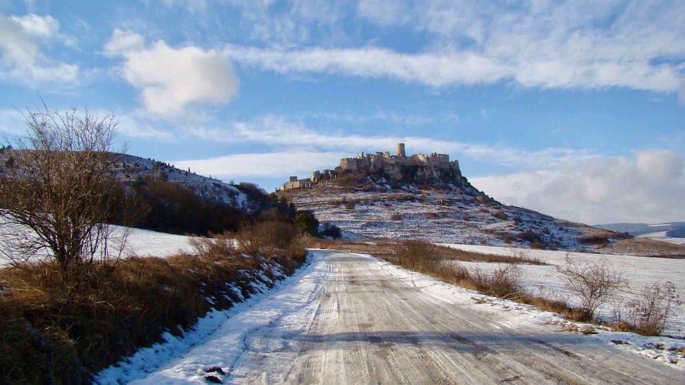 Eine schneebedeckte Straße führt zu einer historischen Burg auf einem Hügel.