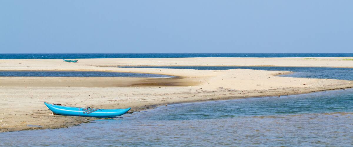 A beach with a blue boat on the shore and calm waters.