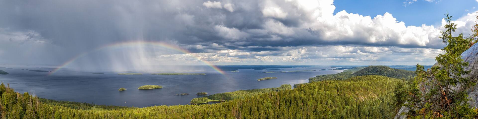 panorama view of Pielina Lake and islands in Koli National Park in Finland with a rainbow under an expressive cloudy sky