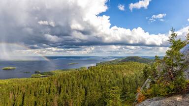 A forested landscape with a lake, islands, and a rainbow.