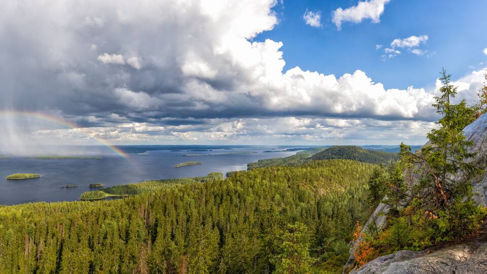 panorama view of Pielina Lake and islands in Koli National Park in Finland with a rainbow under an expressive cloudy sky