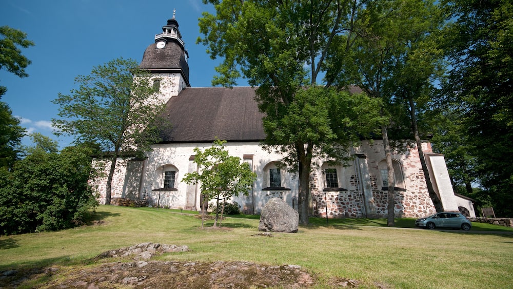 A historic church with a clock tower, surrounded by lush greenery and a stone wall.