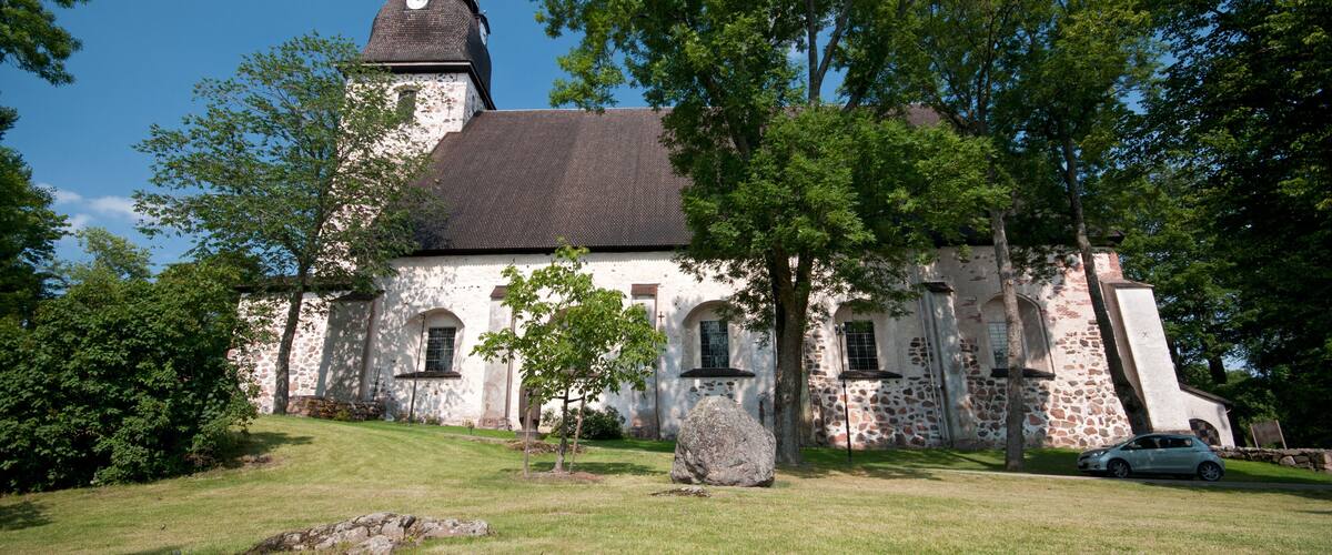 A historic church with a clock tower, surrounded by lush greenery and a stone wall.
