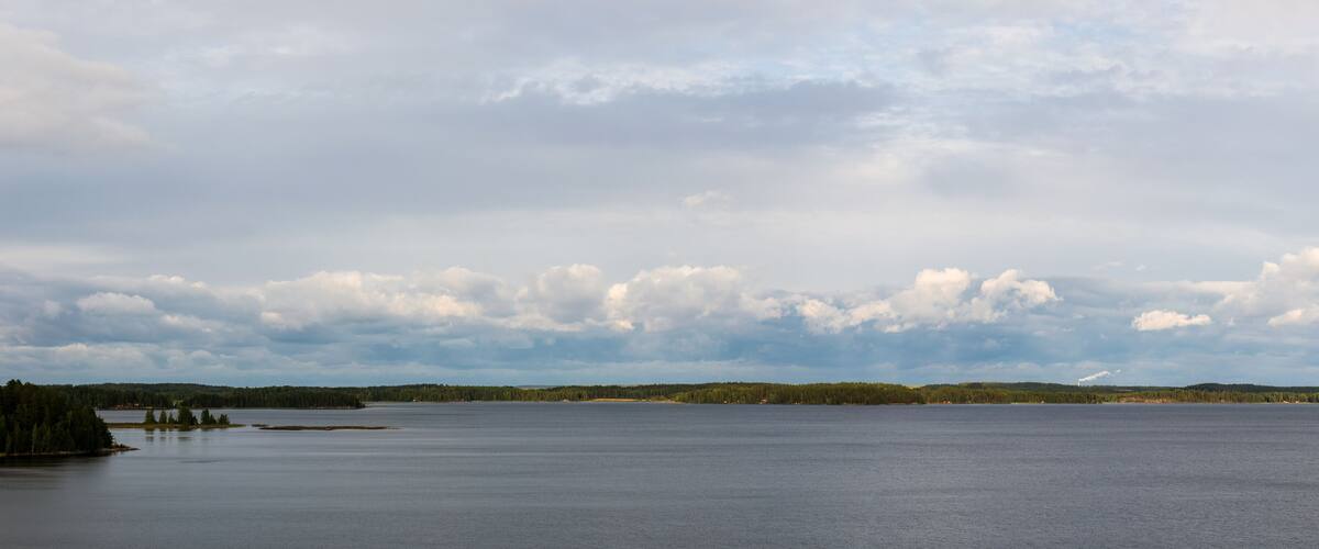 A calm lake with a forested shoreline and a cloudy sky.