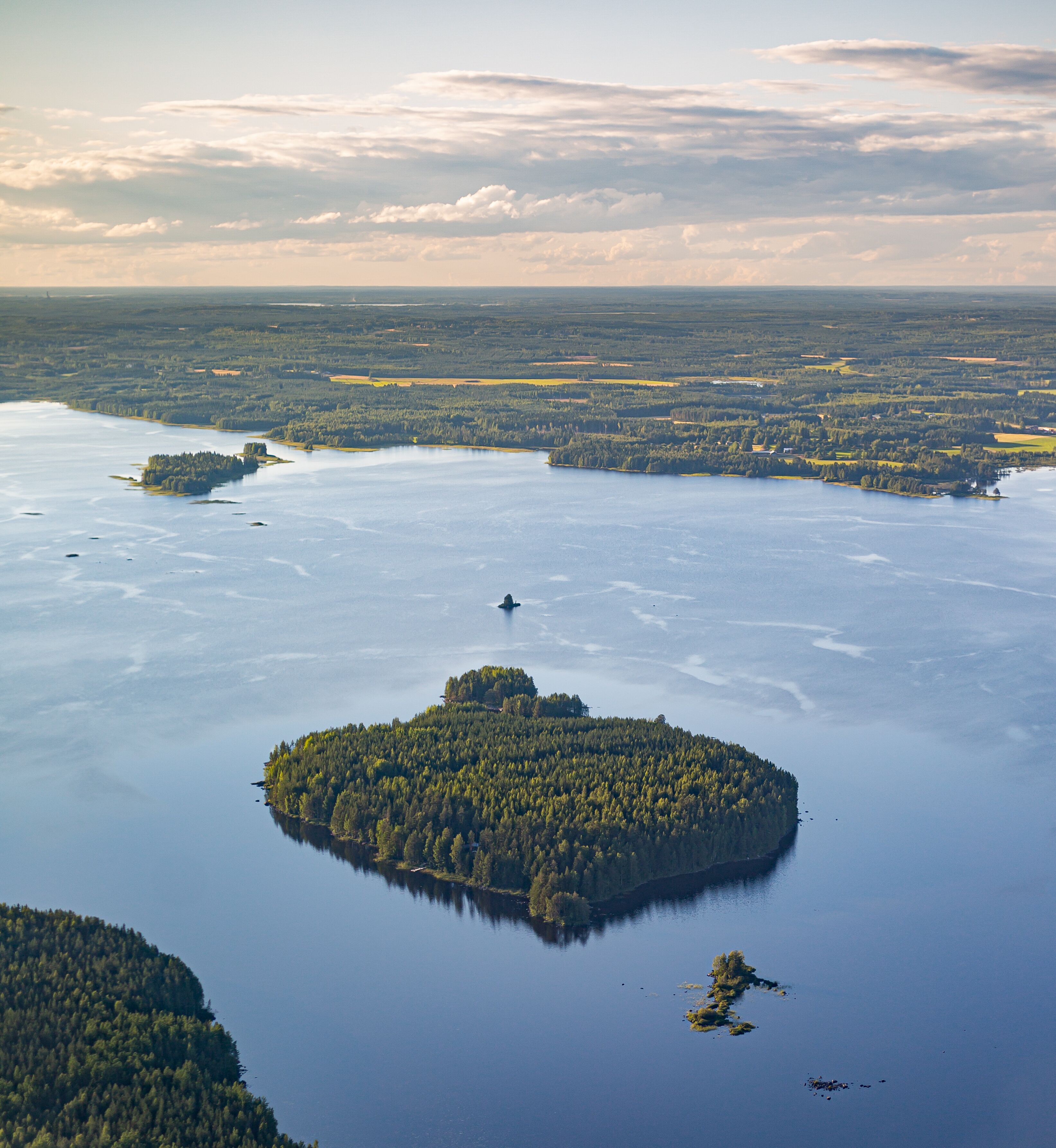 An aerial view of a lake surrounded by forested islands and a distant shoreline.