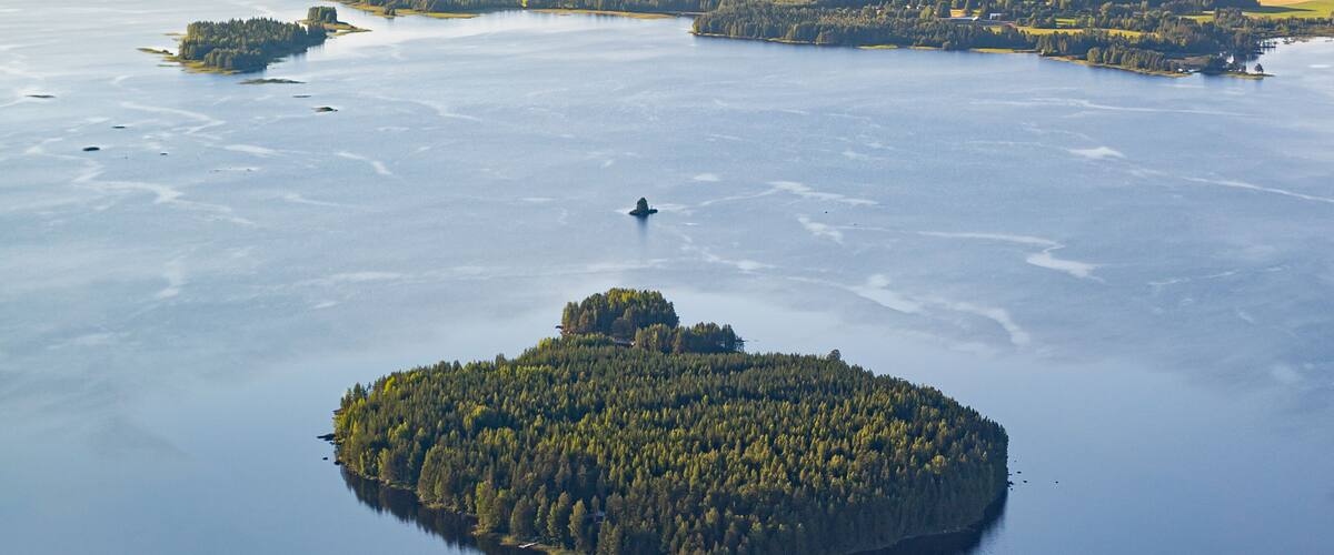 An aerial view of a lake surrounded by forested islands and a distant shoreline.